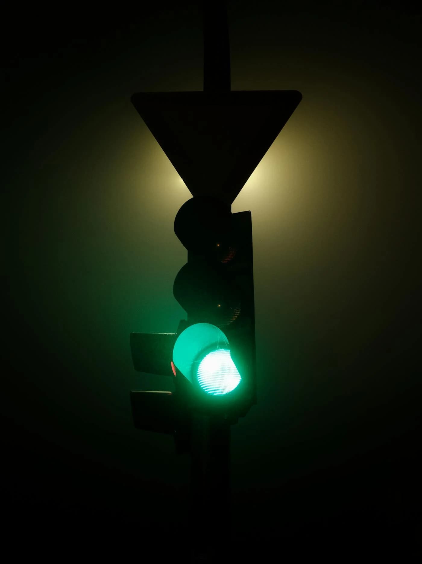 Green traffic light cutting through dense fog