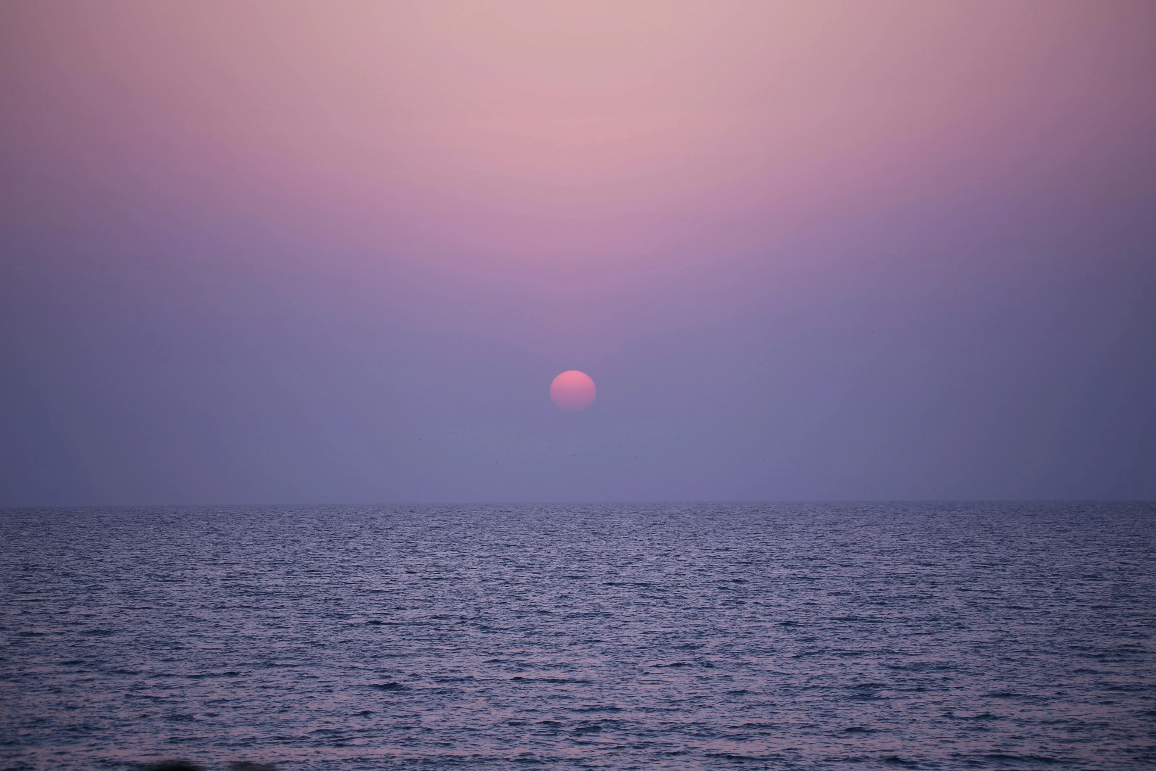 Purple sea horizon with a small sun above the water